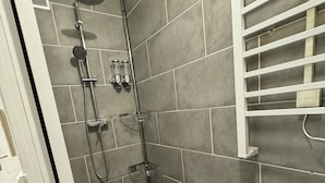 A shower area with grey tiles, a white towel rack, and a showerhead. - Appartement Cosy (Roussillon)