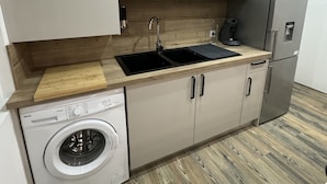 A compact kitchen with a stainless steel microwave, a built-in dishwasher, a sink, and a refrigerator. - Appartement Cosy (Roussillon)