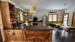 Una cocina moderna con armarios de madera, una isla central con taburetes de bar, una zona de comedor con mesa y sillas, y un amplio ventanal que proporciona luz natural.