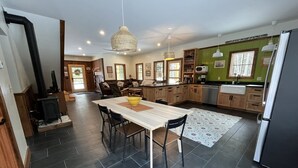 Una cocina moderna con comedor, que presenta un amplio tavolo de madera, suelo de baldosas oscuras y una estufa empotrada.