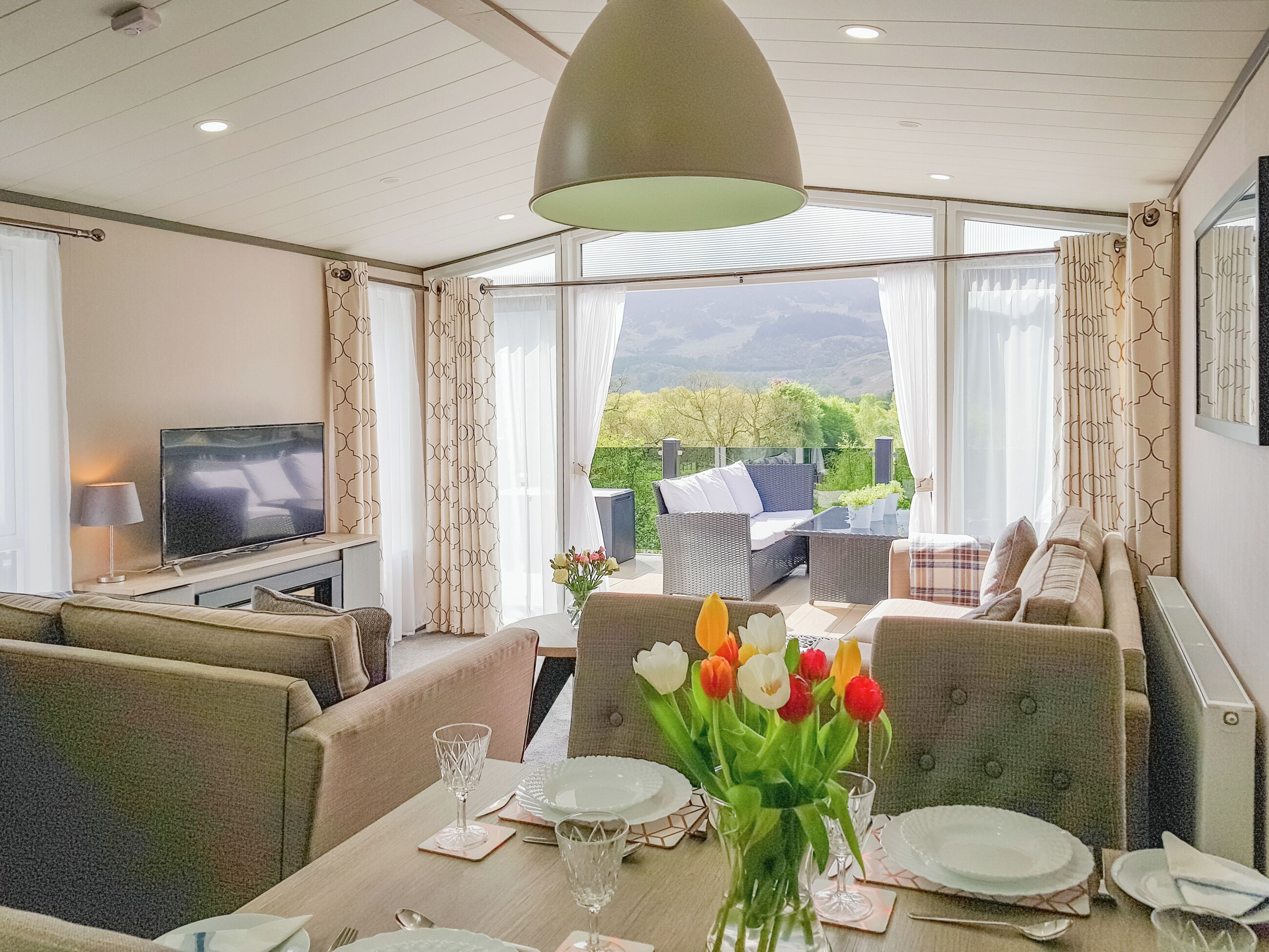 A hotel room with a dining area, a television, and a balcony with outdoor furniture.
