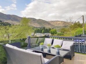 An outdoor seating area with wicker furniture and glass-top tables, overlooking a mountainous landscape.