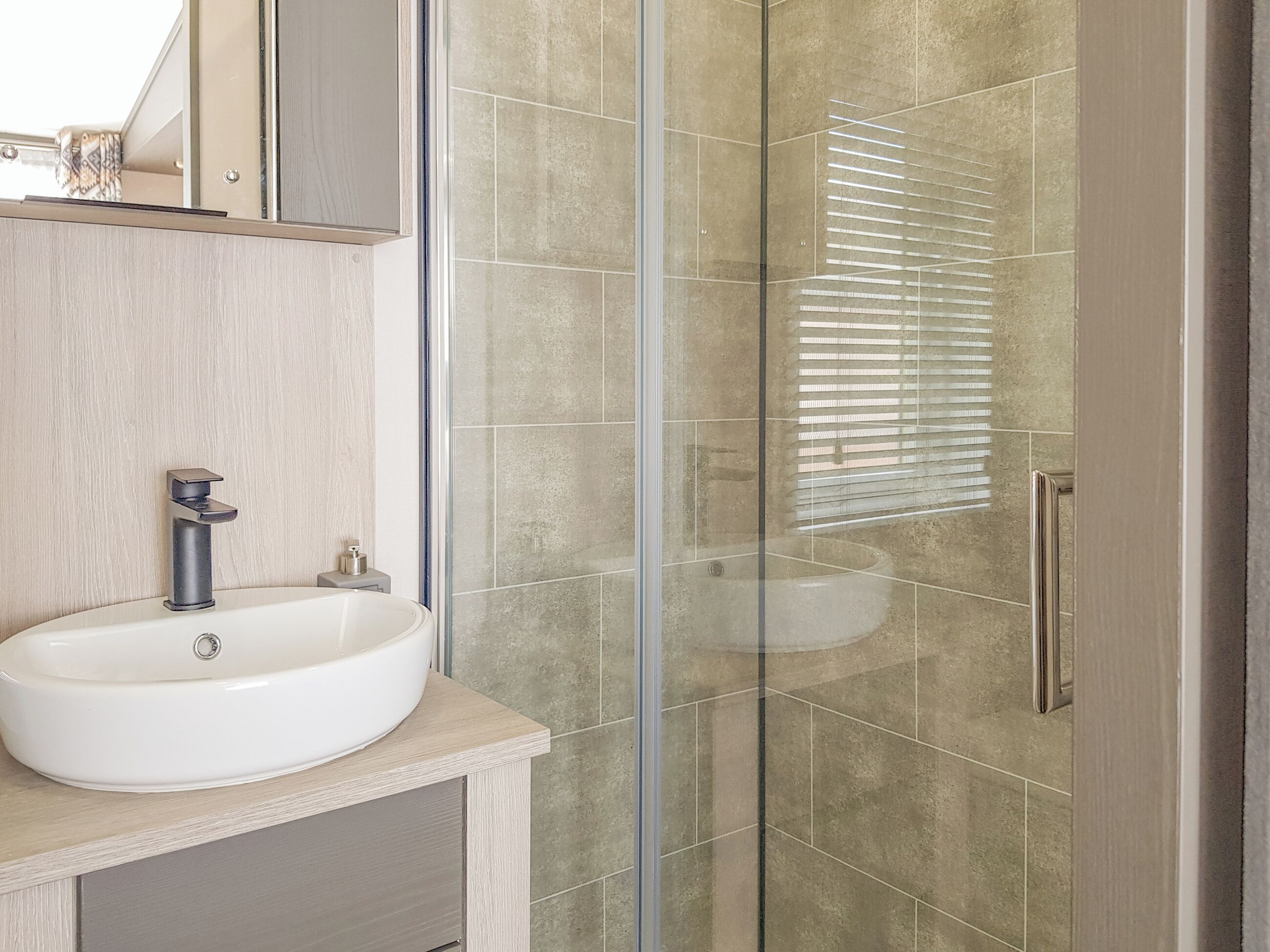 A bathroom with a white sink, a mirror, and a glass shower enclosure.