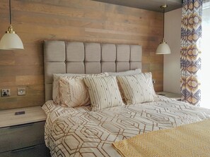 Een moderne slaapkamer met een gestoffeerd hoofdeinde, een bed met een decoratief sprei en een nachtkastje met een lamp.