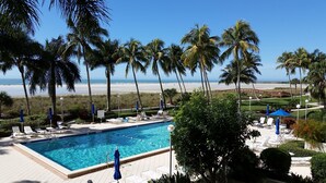 A pool area with lounge chairs and umbrellas, surrounded by palm trees and a view of the beach. - Looking for More than Two Bedrooms on the Beach? (Marco Island)