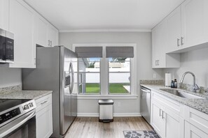 Una cocina moderna con armarios blancos, electrodomésticos de acero inoxidable, un ventanal con vistas y una encimera de granito.