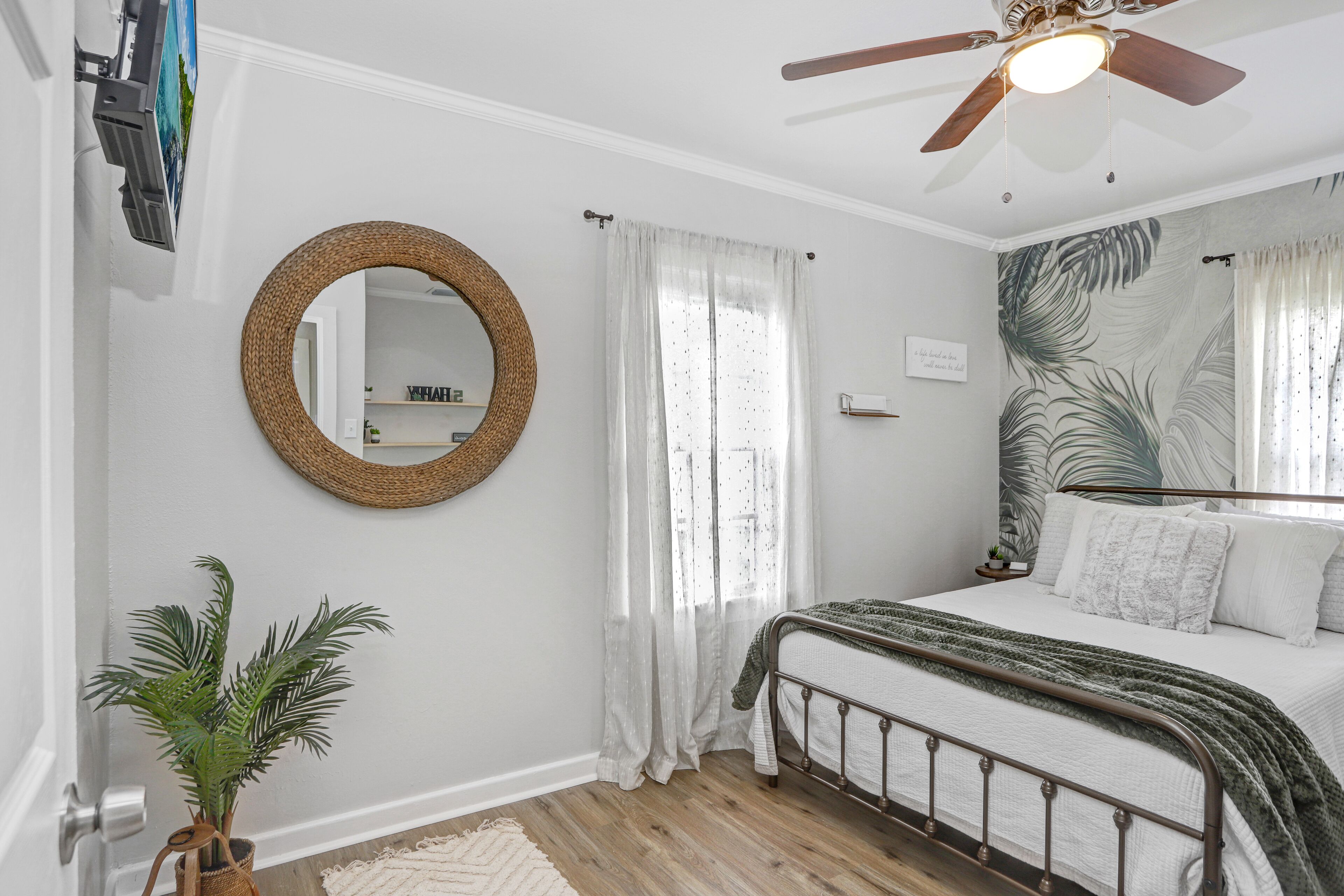 Une chambre à coucher avec un lit, un ventilateur de plafond, un miroir et une plante en pot.