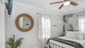 Ein Schlafzimmer mit einem Bett, einem Deckenventilator, einem Spiegel und einer Topfpflanze.