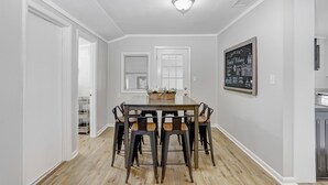 Ein Essbereich mit einem rechteckigen Tisch, der von sechs Stühlen umgeben ist, einer weißen Decke mit eingelassener Beleuchtung und einer gerahmten Kreidetafel an der Wand.