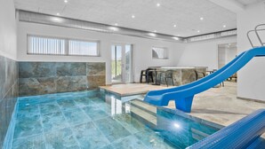 A modern indoor pool with a blue slide, stone walls, and a bar area. - Pet friendly home in Løgstrup with sauna (Løgstrup)