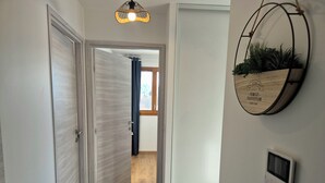 A hallway with a wooden door, a wall-mounted thermostat, and a decorative plant.