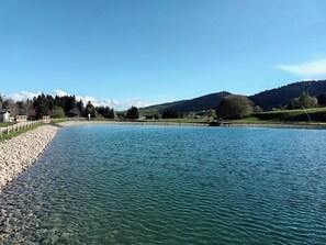 A clear lake with a rocky shoreline, surrounded by hills and sparse vegetation.