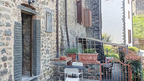 Ein Steinhaus mit einer kleinen Außenbestuhlung, darunter ein Tisch und Stühle, umgeben von Topfpflanzen.
