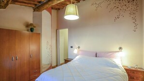 Ein Schlafzimmer mit einem Holzschrank, einem Bett mit weißer Bettdecke, einem Nachttisch mit Lampe und einem an der Wand befestigten Spiegel.