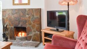 Ein Wohnzimmer mit Kamin aus Stein, einem Fernseher auf einem Holzständer, einem pinken Sessel und einer Lampe auf einem Beistelltisch.