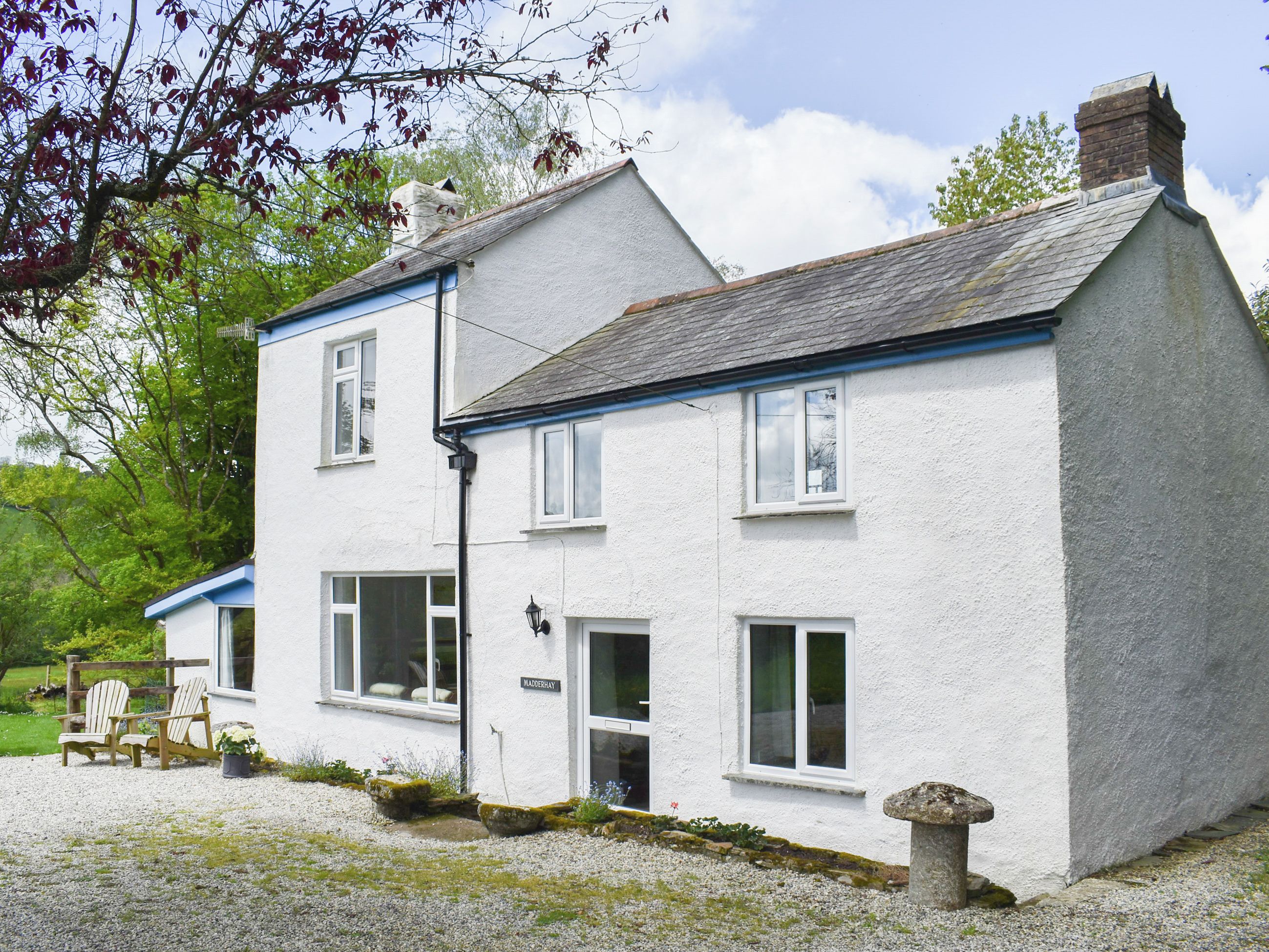 A white two-story house with a blue trim, a chimney, and a gravel driveway.