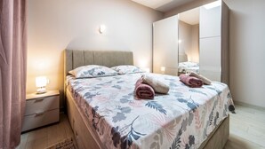 Ein ordentlich bezogenes Bett mit floralem Bettbezug, eine Nachttischlampe und ein Spiegel an der Wand.
