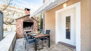 Eine Terrassenausstattung mit einem Grill aus Ziegelsteinen, einem Tisch mit Geschirr und Gläsern sowie einer Tür seitlich.