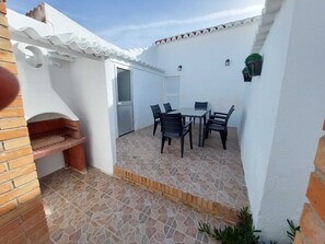 A patio with a brick oven, a table with chairs, and a door leading to an interior space.