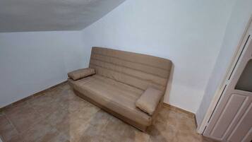 Un sofá color beige en un rincón de una habitación con suelo de baldosas y paredes blancas.