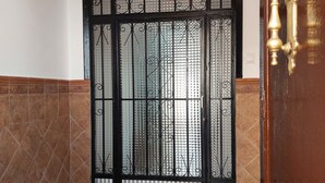 A room with a large, ornate metal gate, tiled walls, and a wooden door with brass handles. - Casa Jaro en el Centro del Pueblo (Sierra de Yeguas)