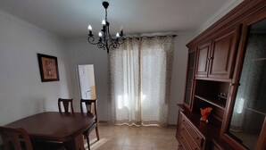A dining area with a wooden table and chairs, a chandelier, a cabinet, and a window with curtains. - Casa Jaro en el Centro del Pueblo (Sierra de Yeguas)