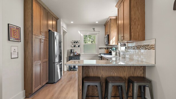 A modern kitchen with wooden cabinets, stainless steel appliances, and a central island with bar stools. - M2 -Relaxed Beach Stay • Fenced Yard, Fire Pit & 2 Living Areas, Pets welcome (Muskegon)
