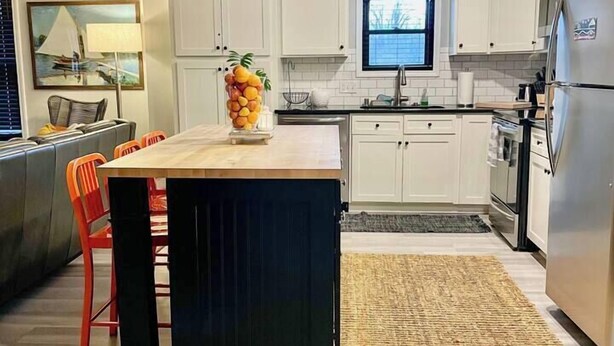 Een moderne keuken met witte kasten, een centraal eiland, een kroonluchter en een eethoek met oranje stoelen.