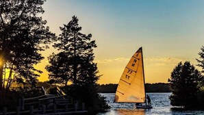 Een zeilboot met een zeil waarop cijfers staan, op een rustig wateroppervlak tijdens zonsondergang.