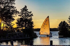Un velero con una vela marcada con números en una superficie acuática tranquila durante el atardecer.