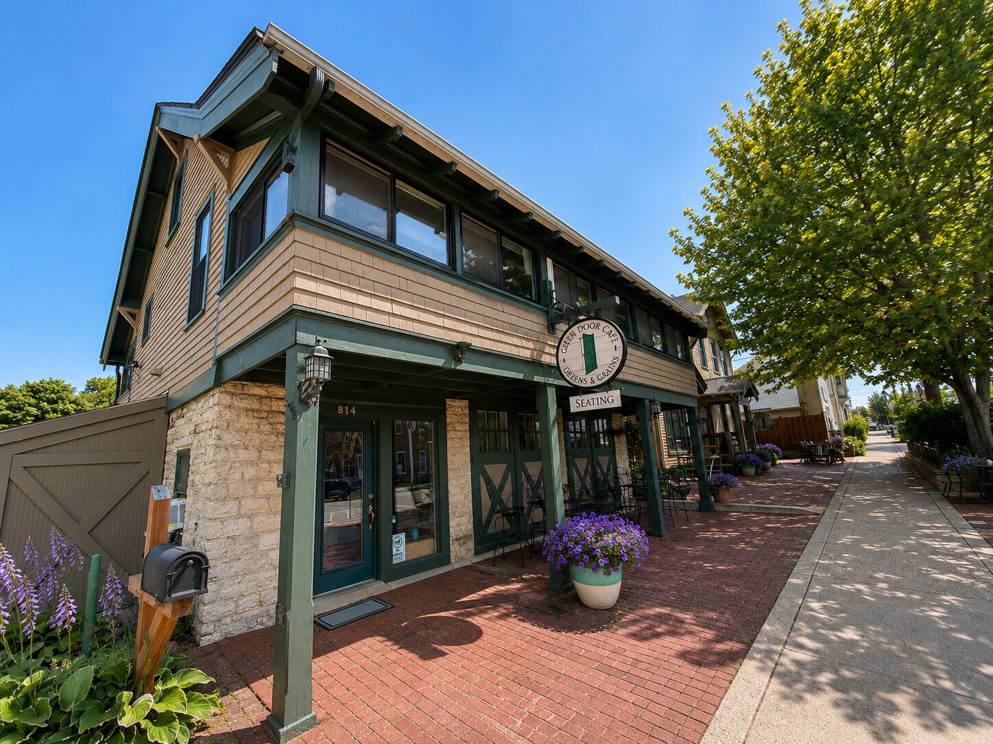 A two-story building with a green door and a sign indicating seating outside.