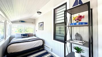 A bedroom with a bed, a window, a shelf with decorative items, and a potted plant.