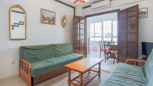 A living room with a green sofa, a wooden coffee table, and a TV. There are two framed pictures on the wall, a window, and a door leading outside. - Gorgeous apartment in Torrevieja (Torrevieja)