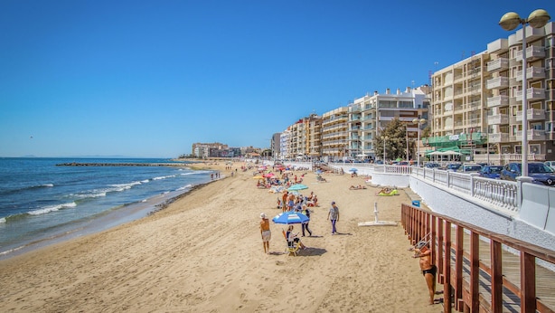A beach with a wooden promenade, beach umbrellas, and people. - Gorgeous apartment in Torrevieja (Torrevieja)