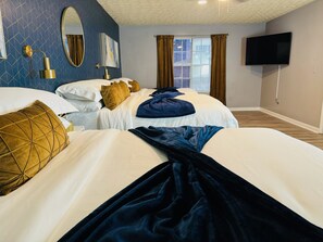 Ett hotellrum med två sängar, en TV, en spegel och ett fönster med gardiner.