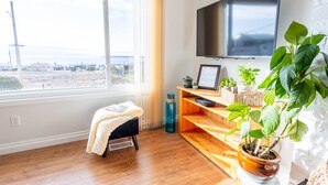 Ein modernes Wohnzimmer mit großem Fenster, Flachbildfernseher, Holzregalen und einem Topfpflanzen.
