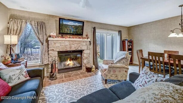 A cozy living room with a stone fireplace, comfortable seating, a television, and a large window overlooking a scenic view.