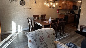 A dining area with a wooden table and chairs, a chandelier, and a wall with decorative items including a clock and a sign that says "hello".