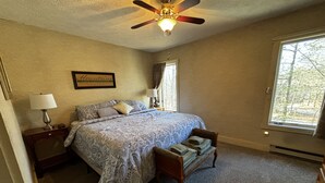 A bedroom with a bed, a nightstand, a lamp, a ceiling fan, a window, and a framed picture on the wall.