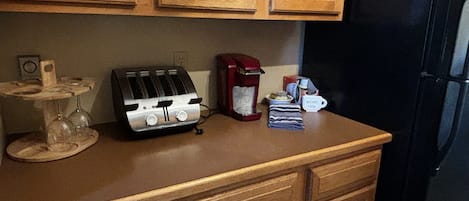 A kitchen with wooden cabinets, a toaster, a coffee maker, and a small table with a glass and a cup.