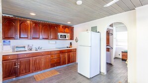 A kitchen with wooden cabinets, a white refrigerator, a microwave, and a sink. - Ocean Mist - AppleSurf! Beachfront one bedroom in Apple Bay (West End Tortola)