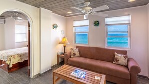 A cozy room with a wooden ceiling, a brown sofa, a wooden coffee table, and a bed with a floral bedspread. - Ocean Mist - AppleSurf! Beachfront one bedroom in Apple Bay (West End Tortola)