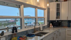 Una cocina moderna con armarios blancos, un ventanal grande y luces colgantes.