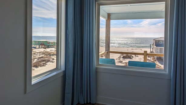 Habitación con un amplio ventanal con vista a la playa, que cuenta con una terraza de madera y vistas al océano.