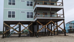 Un edificio de varios pisos con estructura de madera y una playa arenosa al frente.