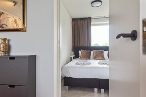 A bedroom with a bed, a nightstand, a dresser, and a window with curtains.
