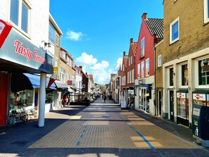 A narrow street lined with traditional buildings, shops, and a visible 'Tasty Corner' restaurant.