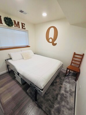 A bedroom with a bed, a chair, a wall-mounted letter 'Q', a window with blinds, and a ceiling vent. - Spotless, Family-Friendly Gem! Hot Tub, Steam Shower, Playground & Gym (Lafayette)