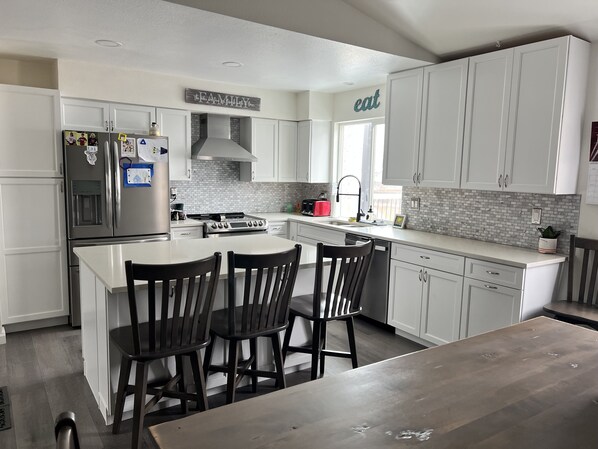 A modern kitchen with white cabinets, a stainless steel refrigerator, a gas stove, and a large island with bar stools. - Spotless, Family-Friendly Gem! Hot Tub, Steam Shower, Playground & Gym (Lafayette)