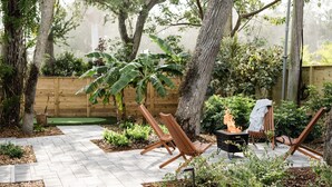 Un patio con dos sillas de madera, un pequeño hogar para fuego y una cerca de madera.